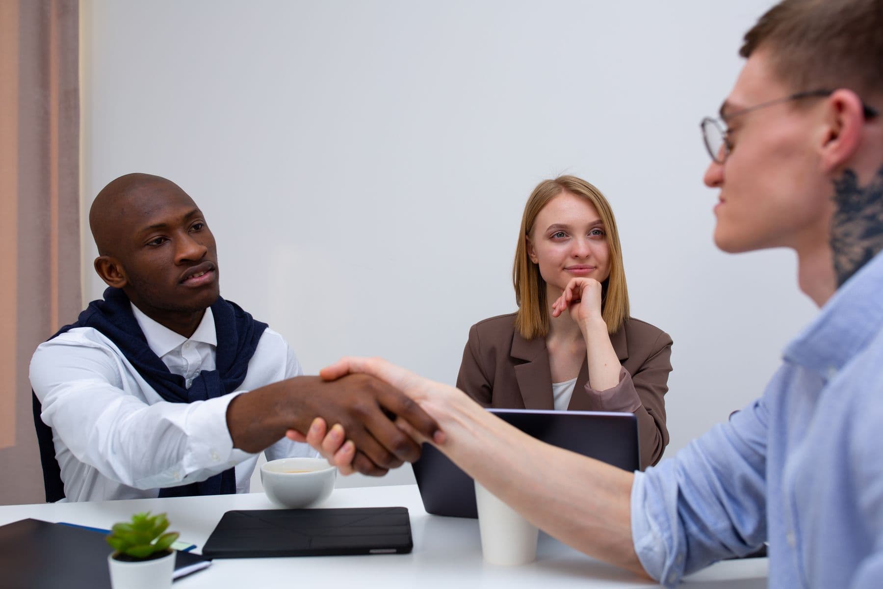 Two professionals from different organisations shaking hands across a meeting table.
