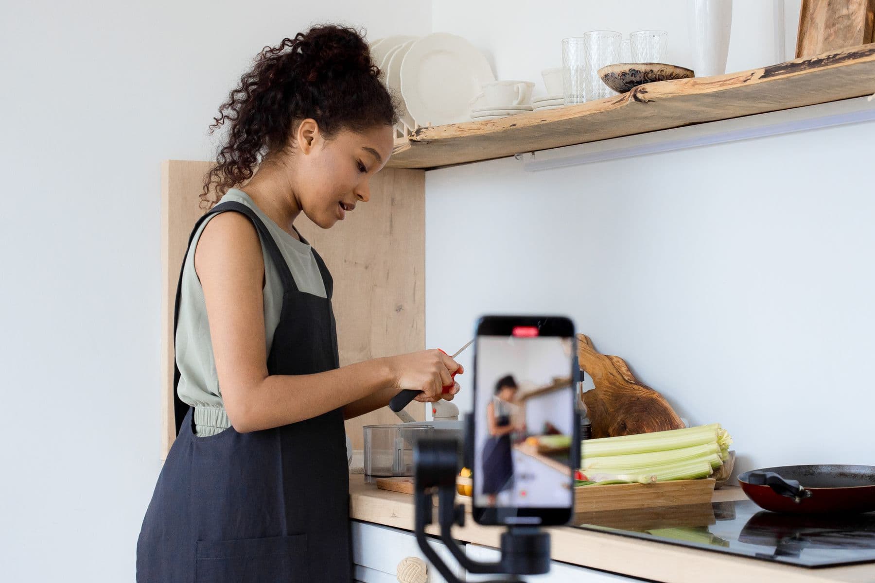 A woman recording community education content on her phone in a bright kitchen.